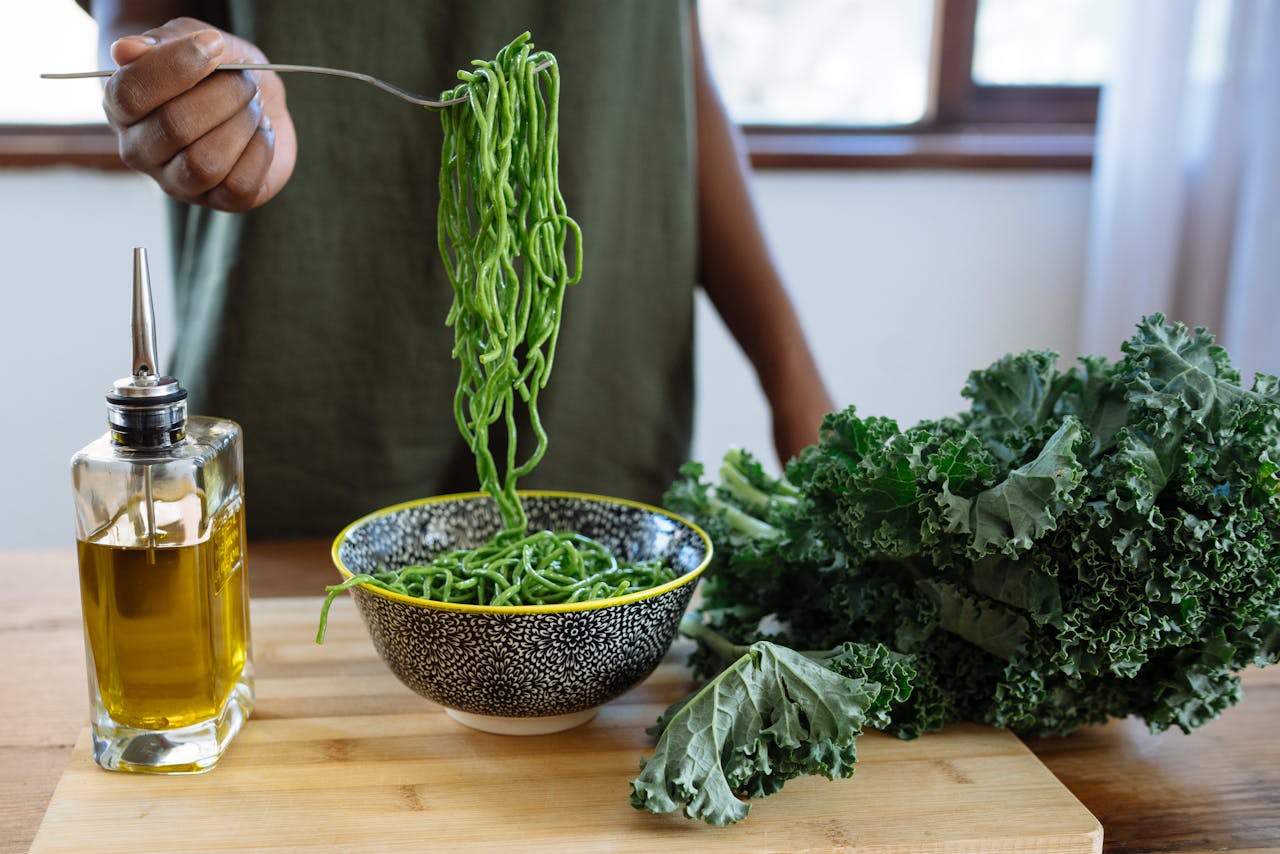 why-choose-us Fresh green kale noodles in a bowl with olive oil on a wooden table. Perfect for a healthy meal.