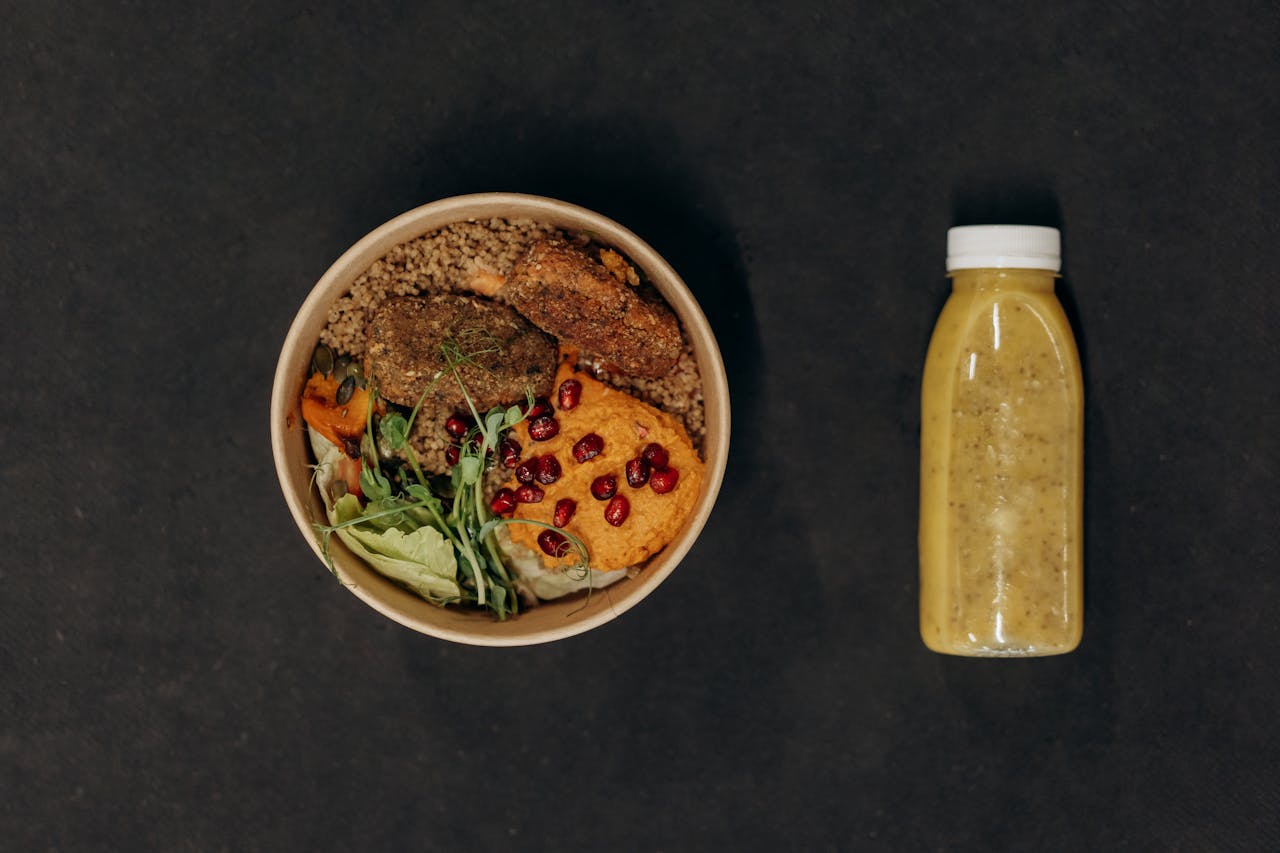 our-services-1 A vibrant vegan bowl with quinoa, fresh vegetables, and a smoothie bottle against a dark backdrop.
